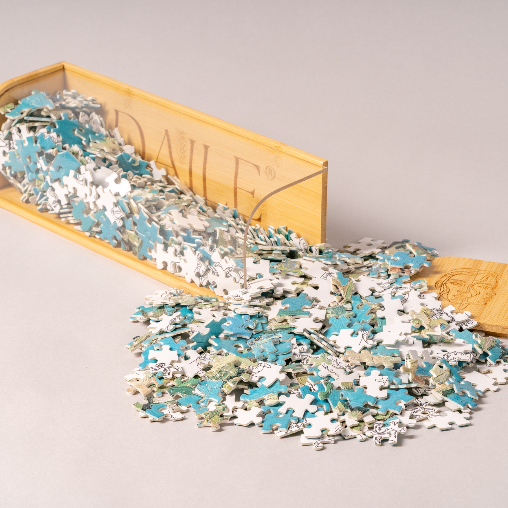 Loose blue and white jigsaw puzzle pieces spilling from a bamboo storage box on a light surface