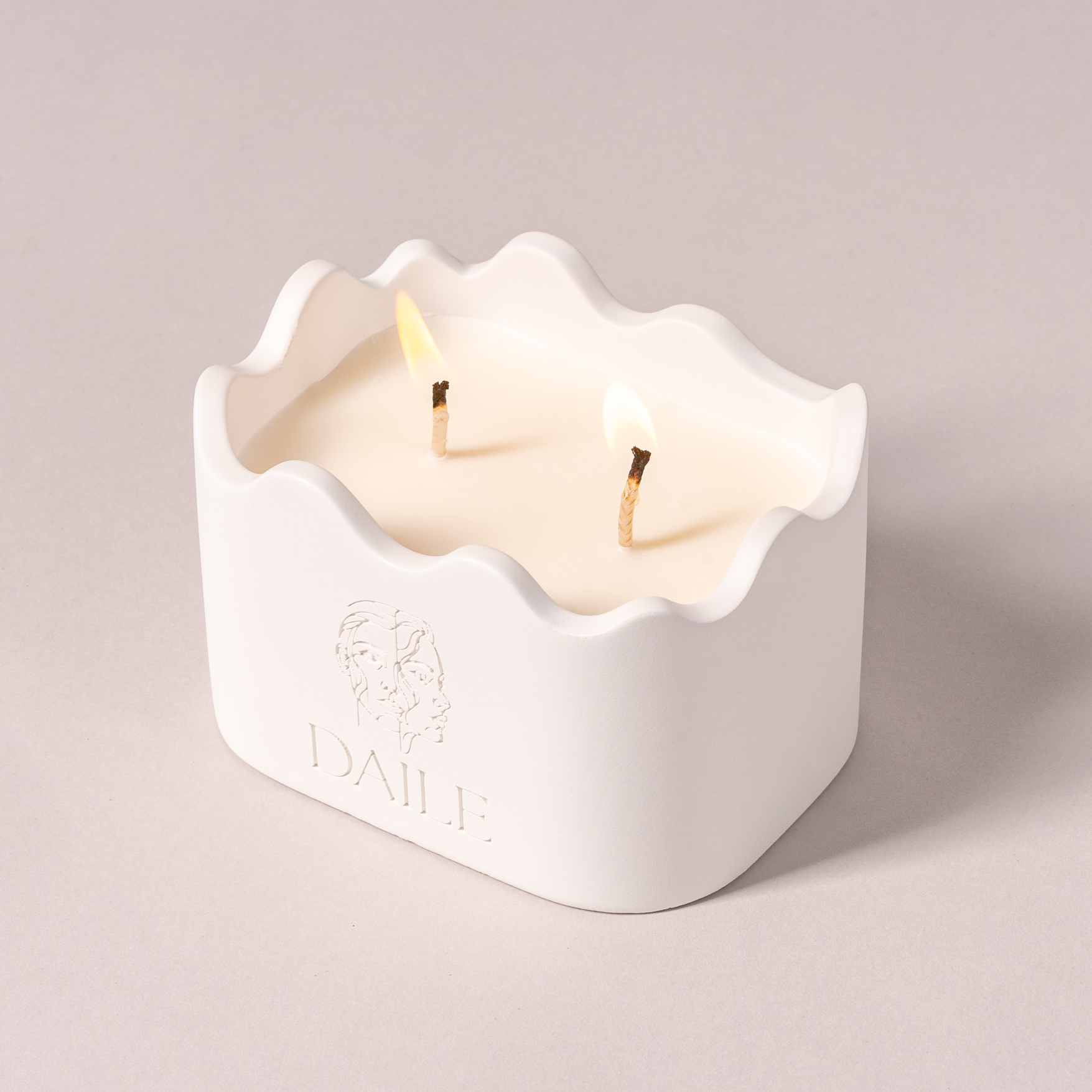 White ceramic candle with two wicks, wavy rim, and minimalist embossed face design