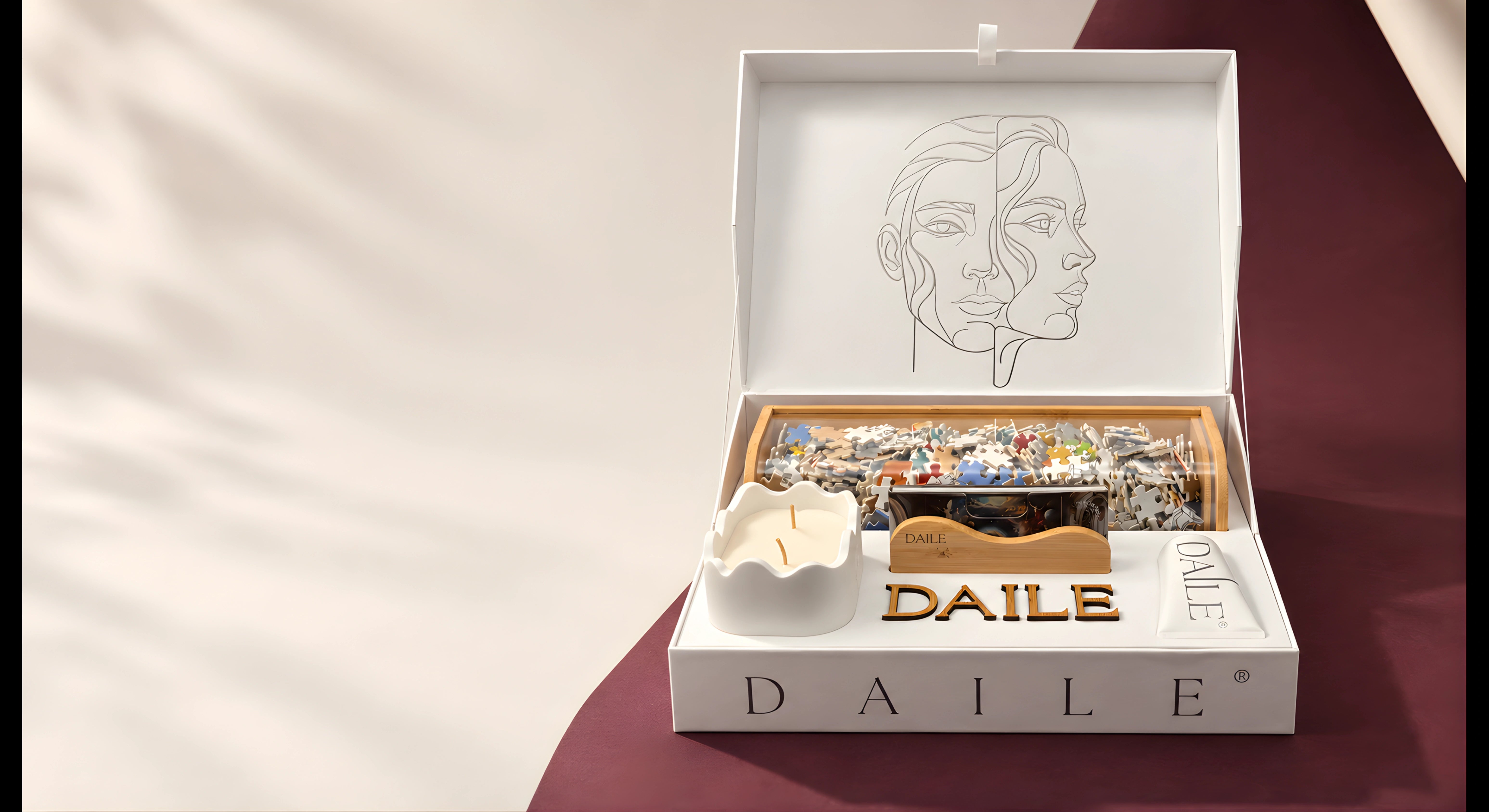 Open DAILE Signature gift box with a puzzle, candle and display accessories on milk-coloured and burgundy paper.